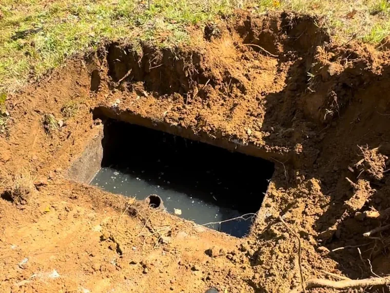 Gloved SepticRooter technician pointing into an excavated septic tank